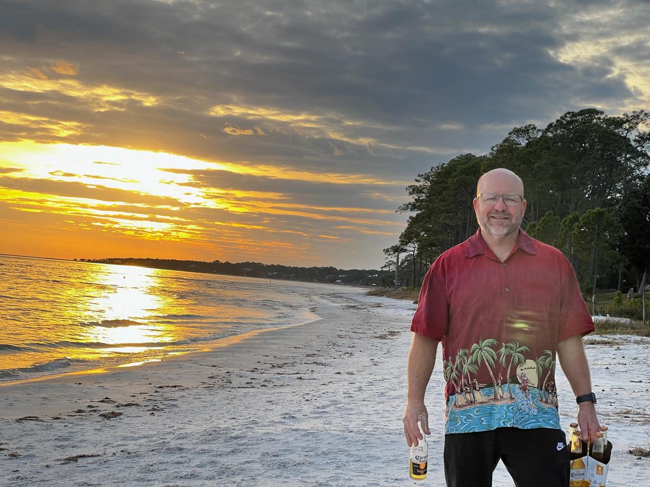 A man standing on the beach with a drink.